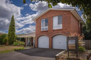 A two-story brick house with a covered patio, two garage doors, and a well-maintained lawn.