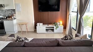 Un salon moderne avec un téléviseur à écran plat, un canapé, une petite table et un coin cuisine à l’arrière-plan.