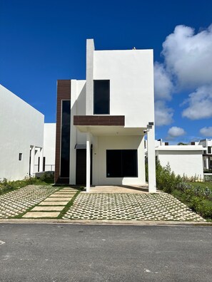 Una casa moderna de dos pisos con techo plano, ventanas amplias y entrada pavimentada.