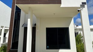 Une maison moderne à deux étages, dotée d’un toit plat, d’une grande fenêtre et d’un petit balcon.