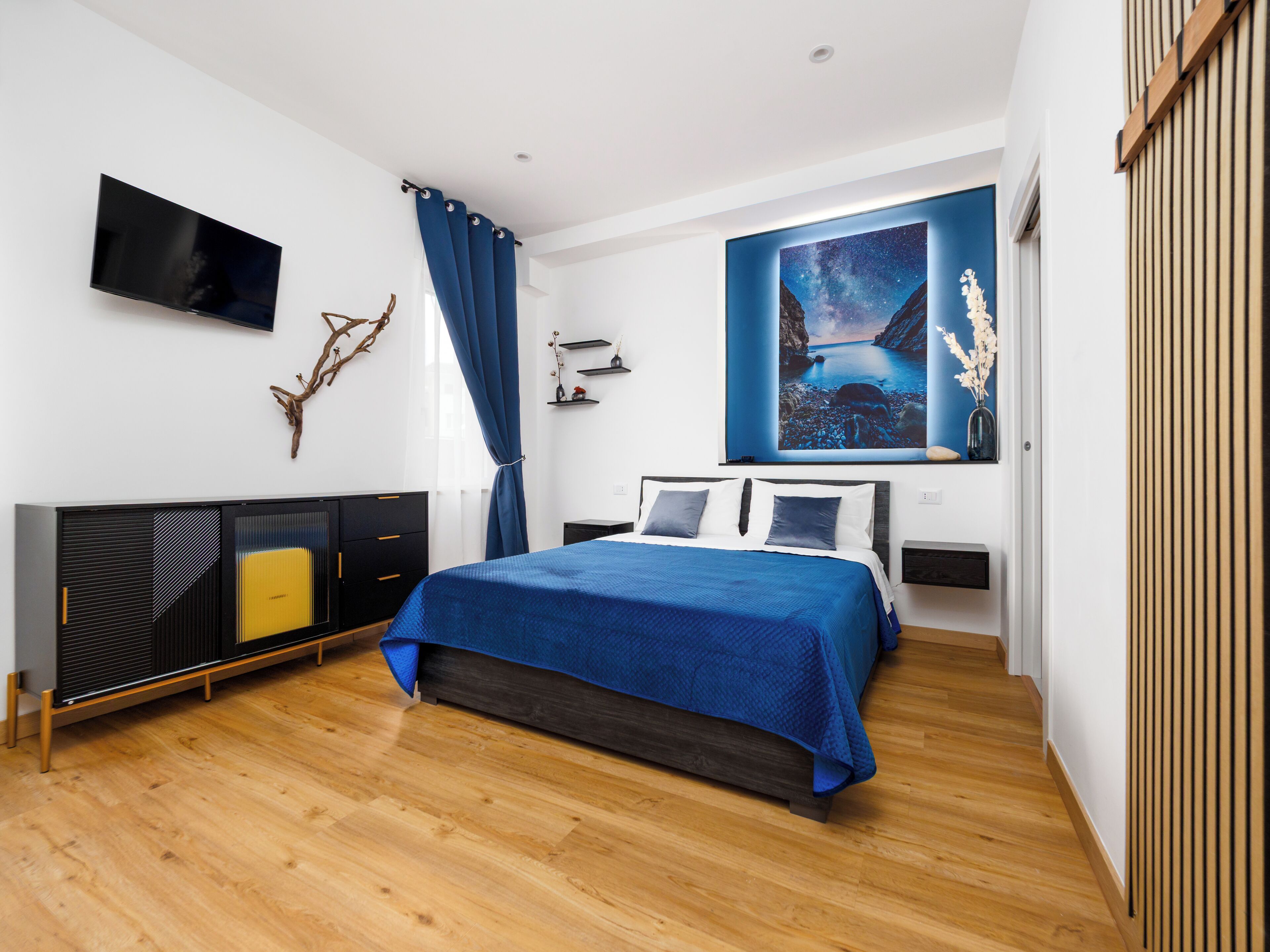 Un dormitorio moderno con cama, televisor de pantalla plana, un cuadro grande y suelo de madera.