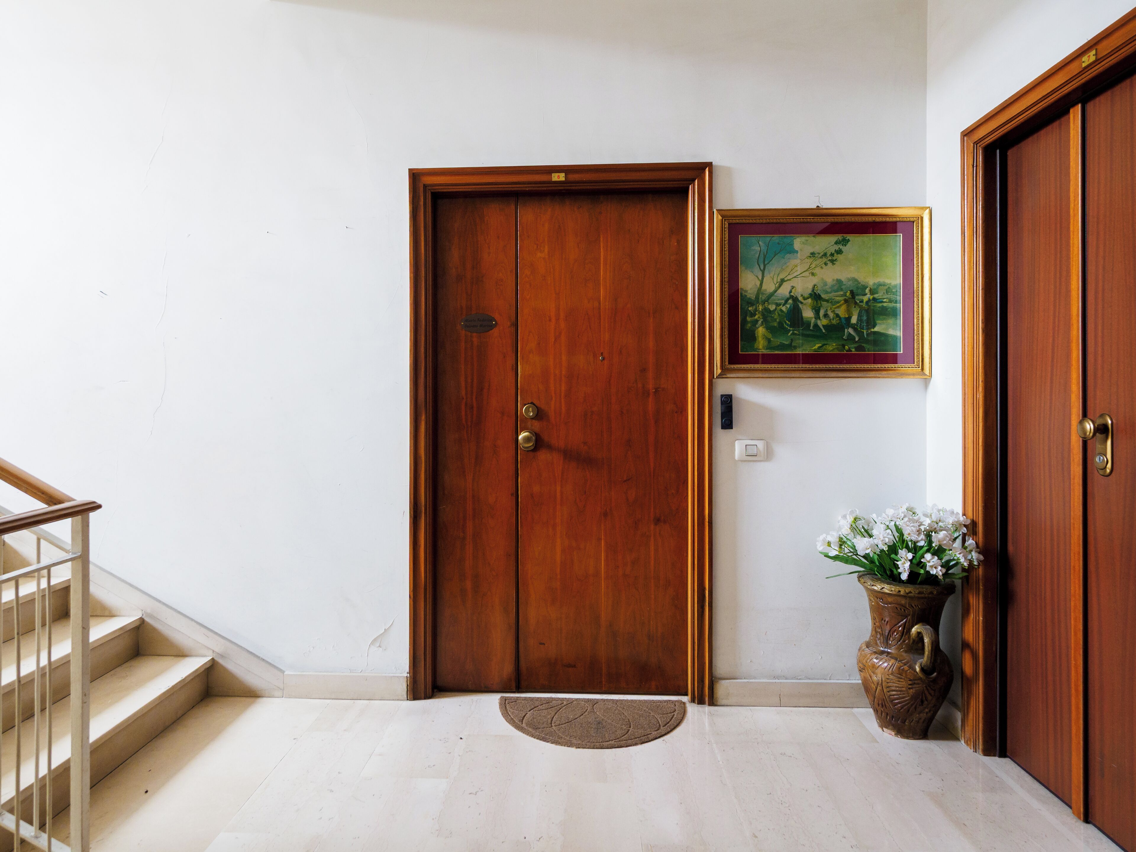 A wooden door with a brass handle, a framed painting above it, a potted plant, and a staircase to the left.