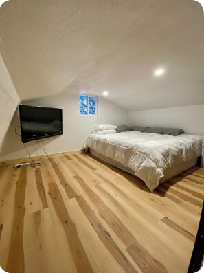 An attic bedroom with a bed, a TV, wooden flooring, and a small window.
