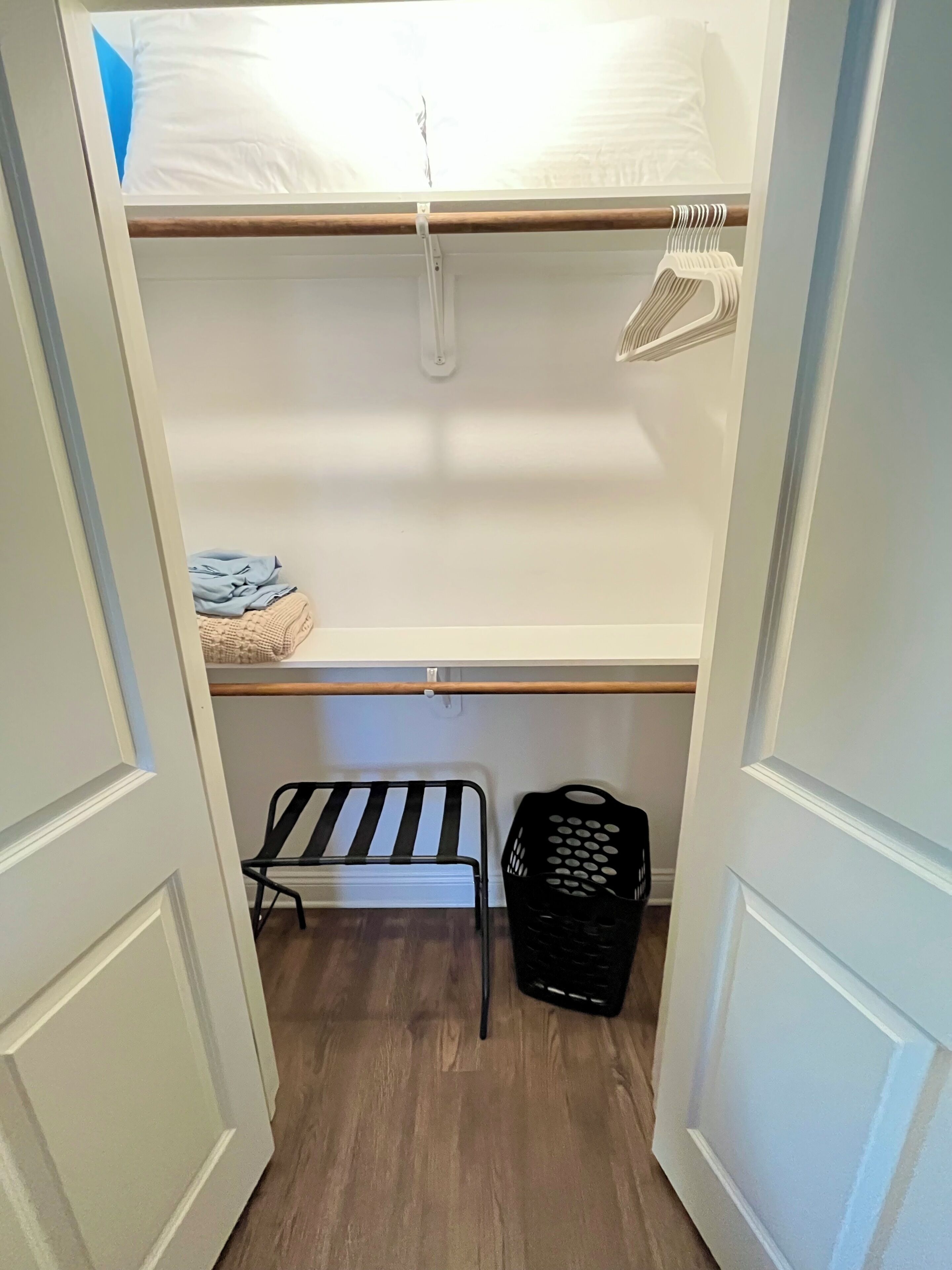 A closet with a bed, a hanging rack, a chair, and a laundry basket.