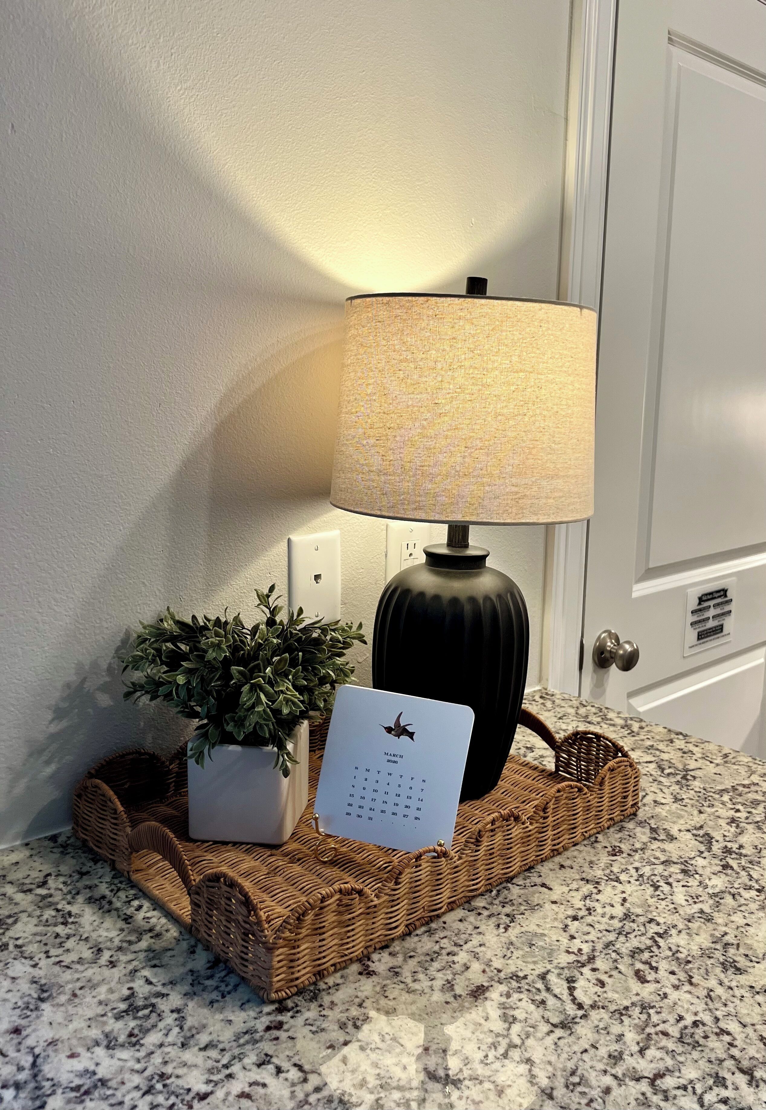 Een lamp, een potplant en een kalender op een geweven dienblad op een granieten aanrecht.