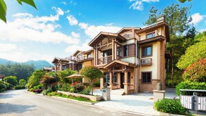 A multi-story hotel with balconies, a landscaped garden, and a mountainous backdrop. - Pandora Valley Villas (Zhangjiajie)