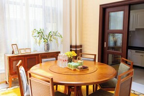 Une table de salle à manger ronde en bois, avec des chaises, un vase rempli de fleurs jaunes, des bouteilles et un plateau de nourriture.