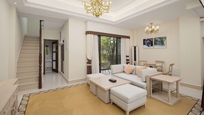 A spacious living area with a sofa, ottoman, and a small table, a staircase, and a large window with curtains. - Pandora Valley Villas (Zhangjiajie)