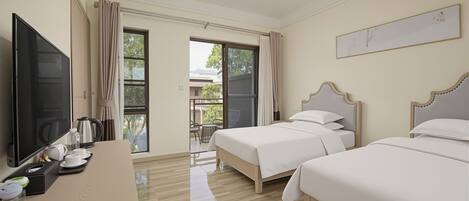 A hotel room with two beds, a TV, a desk with a coffee maker, and a view of the outdoors.