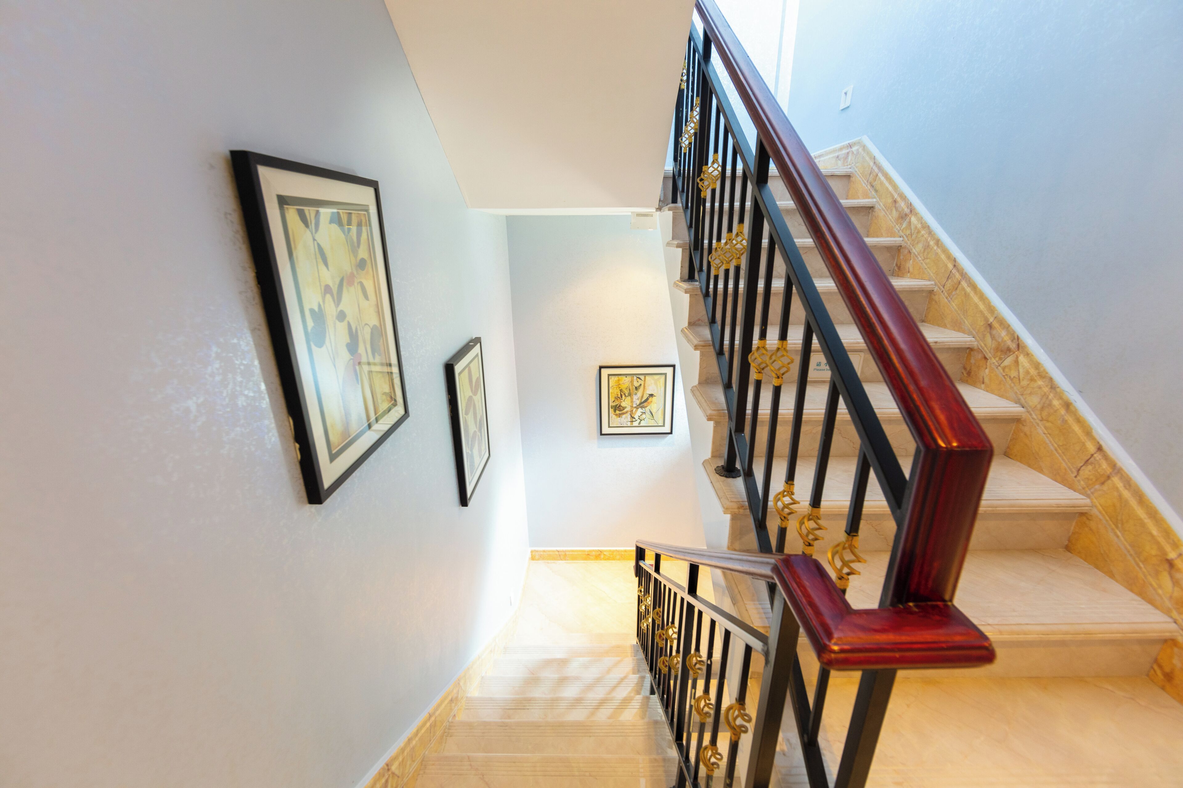 Una escalera con barandilla de madera y balaustres negros, que conduce a una plataforma con cuadros en la pared.