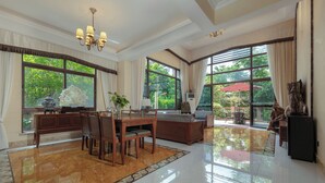 A spacious dining area with a wooden table and chairs, a chandelier, and large windows offering a view of greenery. - Pandora Valley Villas (Zhangjiajie)