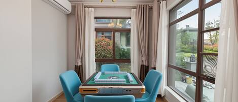 A room with a table, chairs, a chandelier, and large windows.