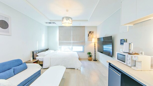 A modern hotel room with a bed, a sofa, a TV, a coffee machine, and a desk.