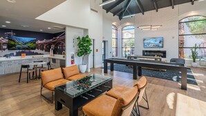 Amplia sala de estar con mesa de fútbol, asientos cómodos, zona de cocina y una gran pantalla de televisión.