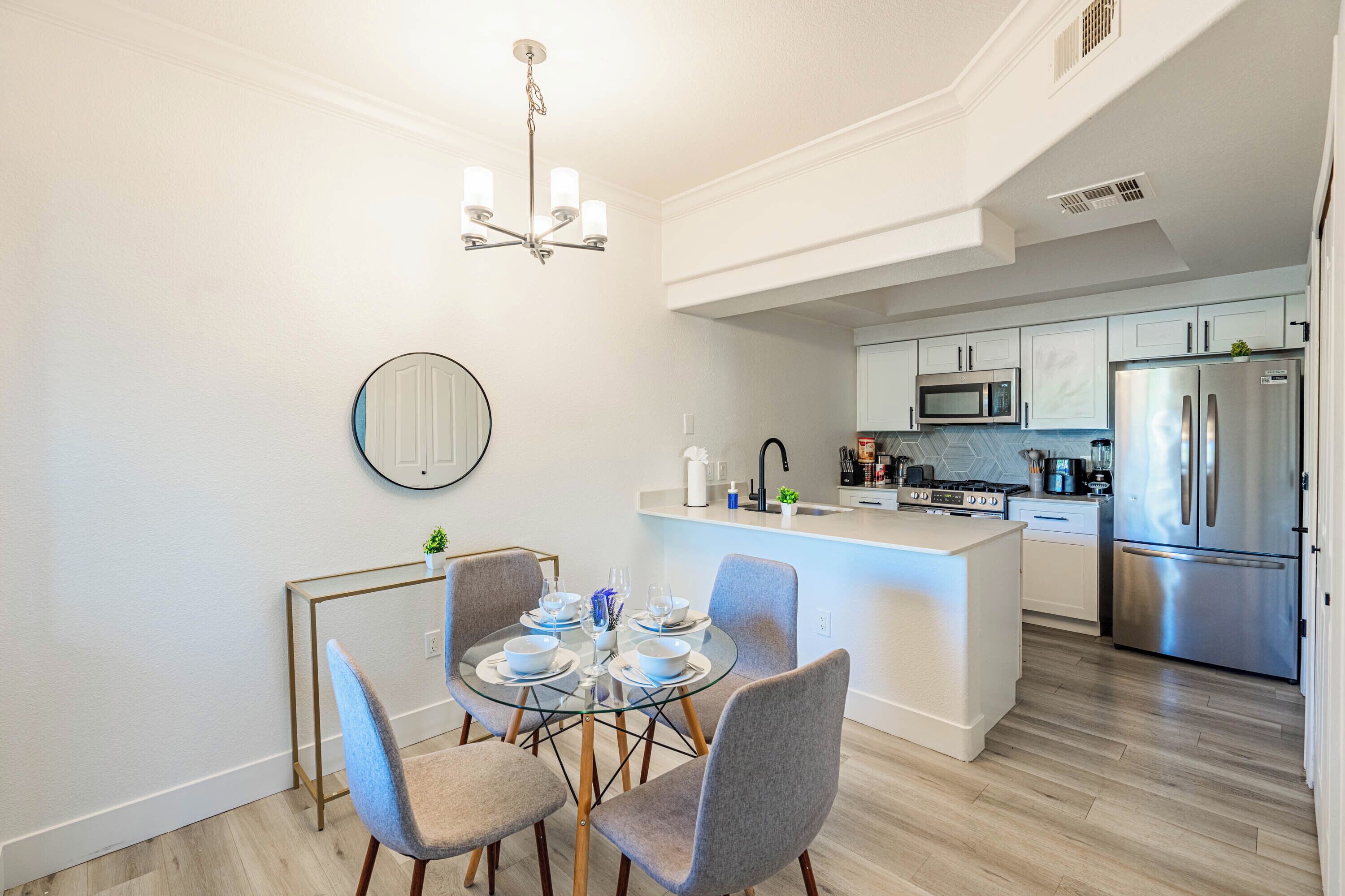 A modern kitchen with stainless steel appliances, a dining area with a glass table, and a small island with a sink.
