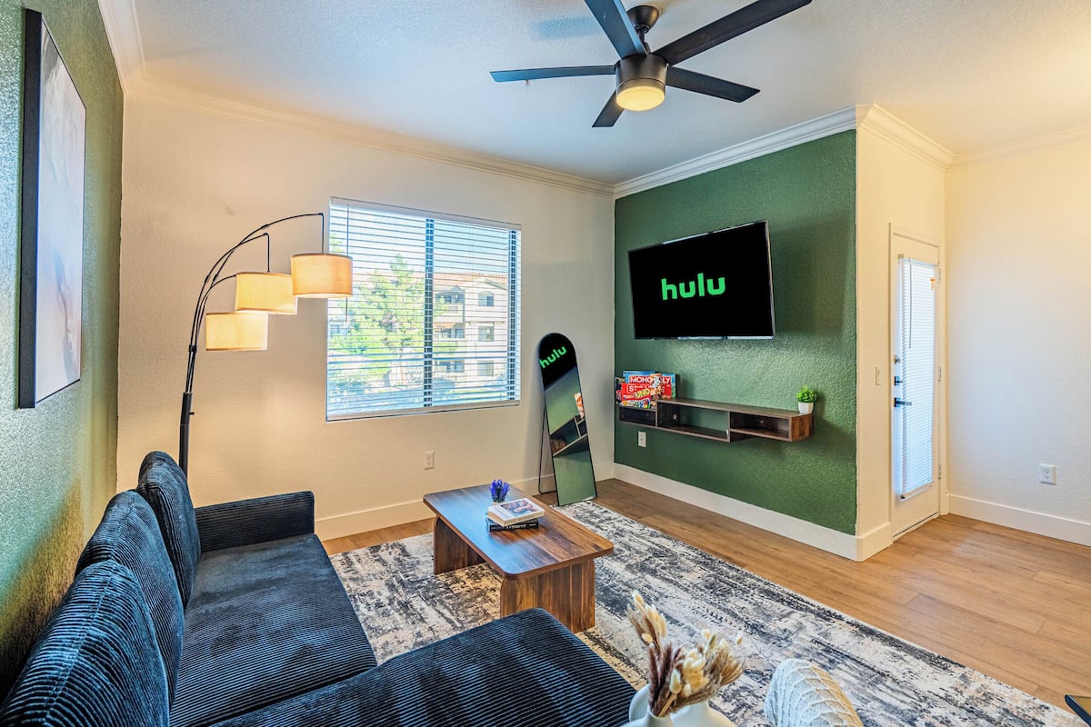 Un salon comprenant un canapé, une table basse, un lampadaire et un téléviseur à écran plat fixé à un mur vert.