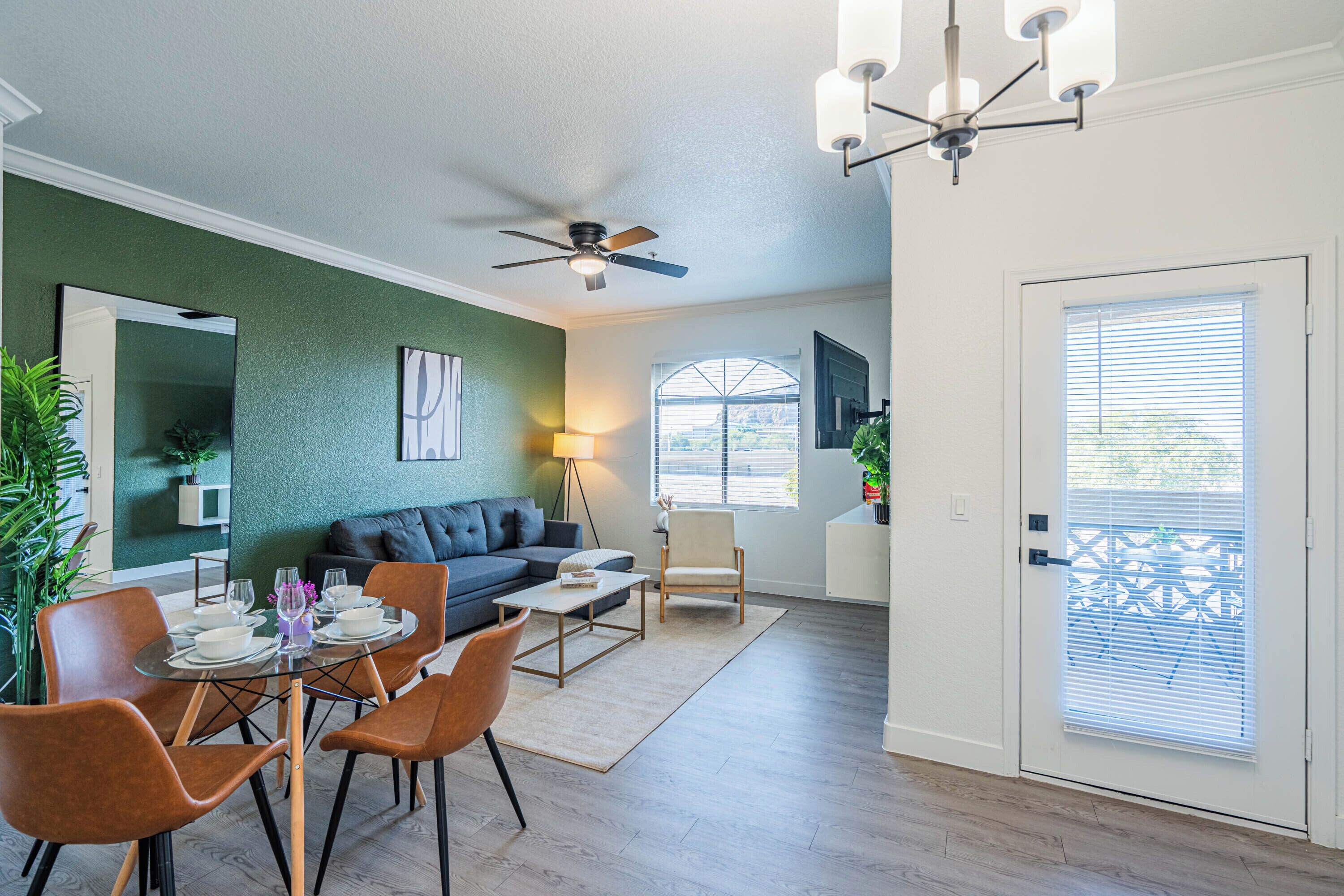 A modern living room with a sofa, dining table, chairs, a ceiling fan, and a door with a window.
