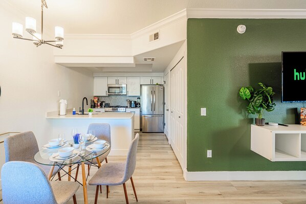 Een moderne keuken met witte kasten, een eethoek met een glazen tafel en stoelen, en een groene accentmuur.