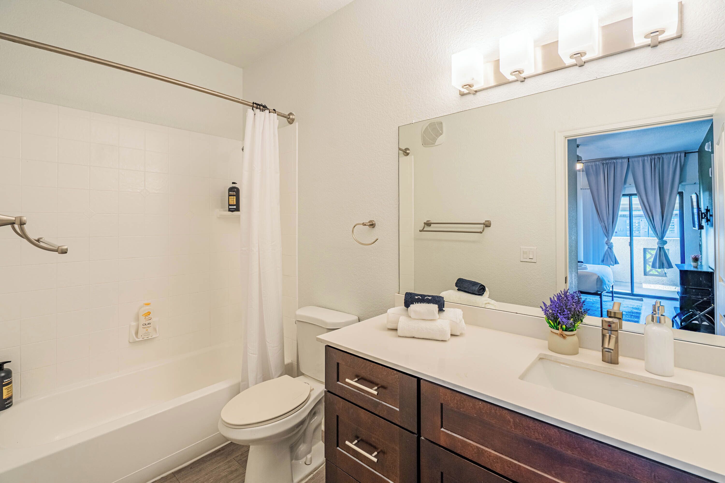 A bathroom with a bathtub, toilet, vanity with a mirror, and a shower curtain.