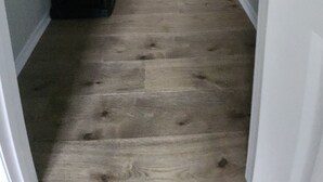 A narrow hallway with a wooden floor, a black metal shelf unit, and white walls. - Bright and cozy condo with inviting vibes for your home away from home (Morehead City)