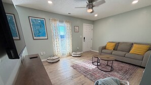 A living room with a sofa, ottomans, a coffee table, a rug, and a television. - Bright and cozy condo with inviting vibes for your home away from home (Morehead City)