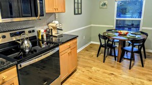 A kitchen with a stove, microwave, and coffee maker, a dining table with chairs, and a window with a view. - Bright and cozy condo with inviting vibes for your home away from home (Morehead City)
