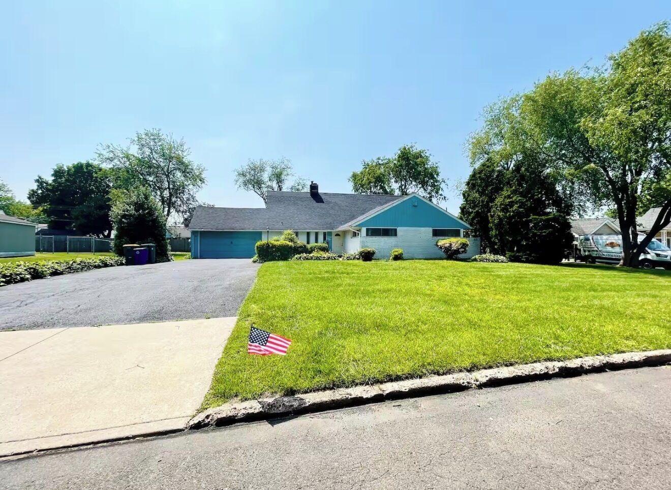 A residential street with a house, a well-maintained lawn, and a flag.