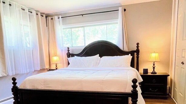 Une chambre à coucher avec un grand lit, deux tables de chevet, une fenêtre avec des rideaux et une porte.