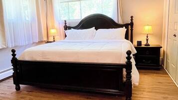A bedroom with a large bed, two bedside tables, a window with curtains, and a door.
