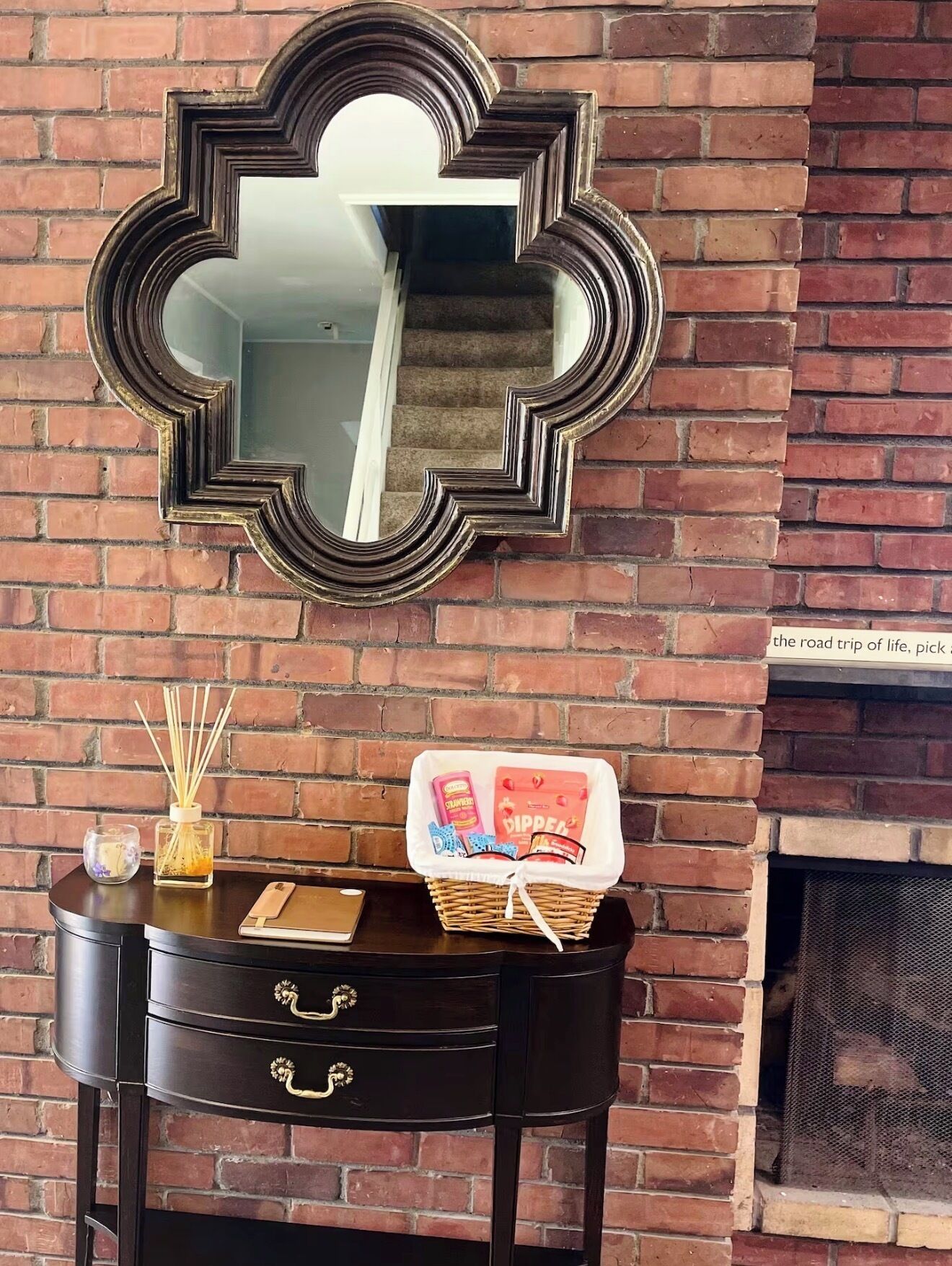 A fireplace with a mirror above it, a black console table with drawers, and a basket with items on it.