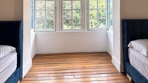 Ein Zimmer mit Holzboden, zwei Betten mit dunklen Kopfteilen und einem Fenster mit Blick auf Grünflächen.