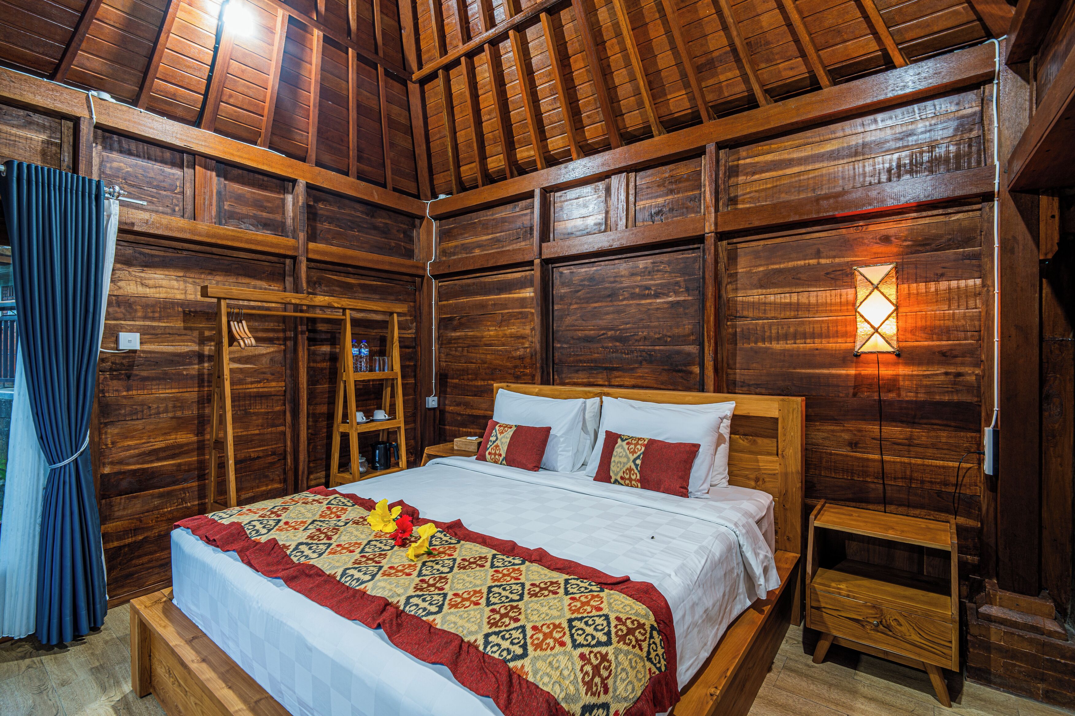 A wooden room with a bed, a nightstand, and a wall-mounted light fixture.