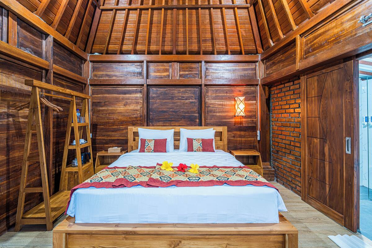 Um quarto de madeira com uma cama, uma escada, um prateleira e uma parede de tijolos.