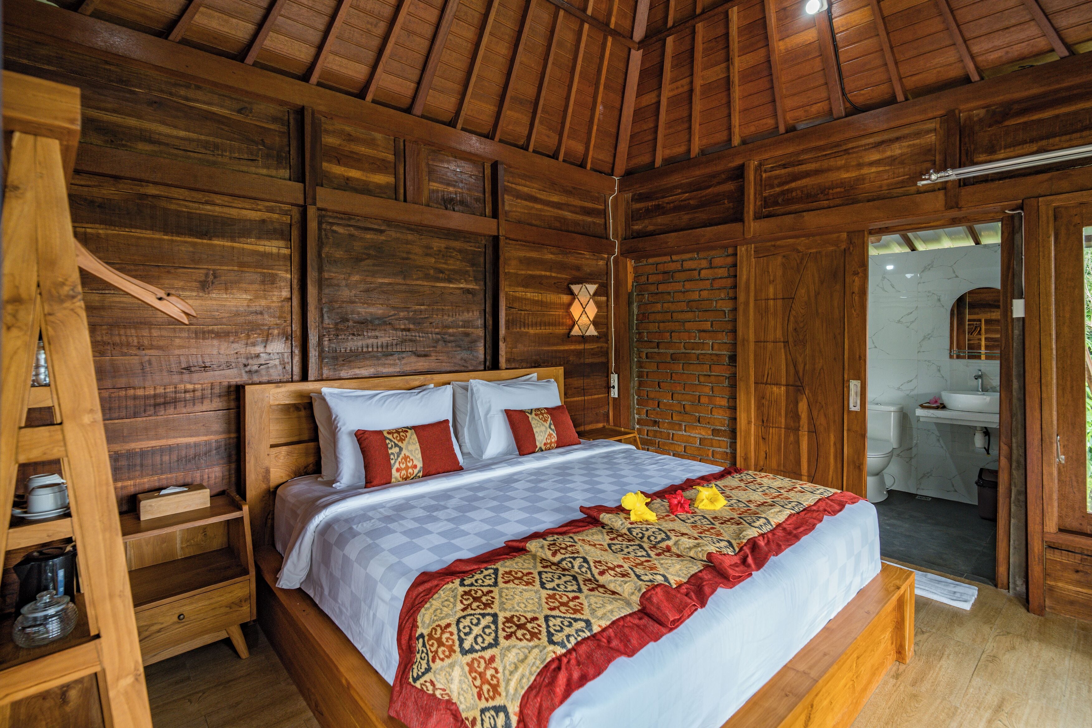 A wooden room with a bed, a wooden ladder, and a bathroom visible through an open door.