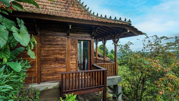 Une maison en bois avec un toit en tuiles, un balcon et une végétation luxuriante tout autour.