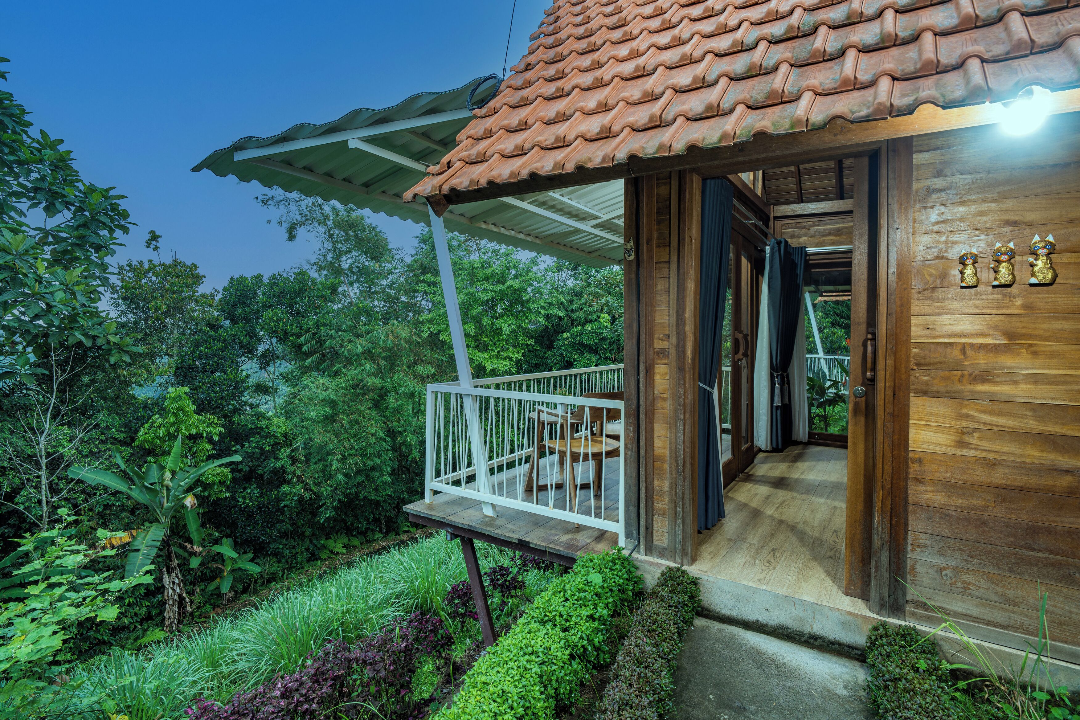 Una casa de madera con techo de tejas, un balcón con barandilla y un jardín con diversas plantas.