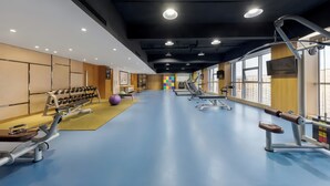 Ein Fitnessraum mit Trainingsgeräten, blauem Boden und großen Fenstern.