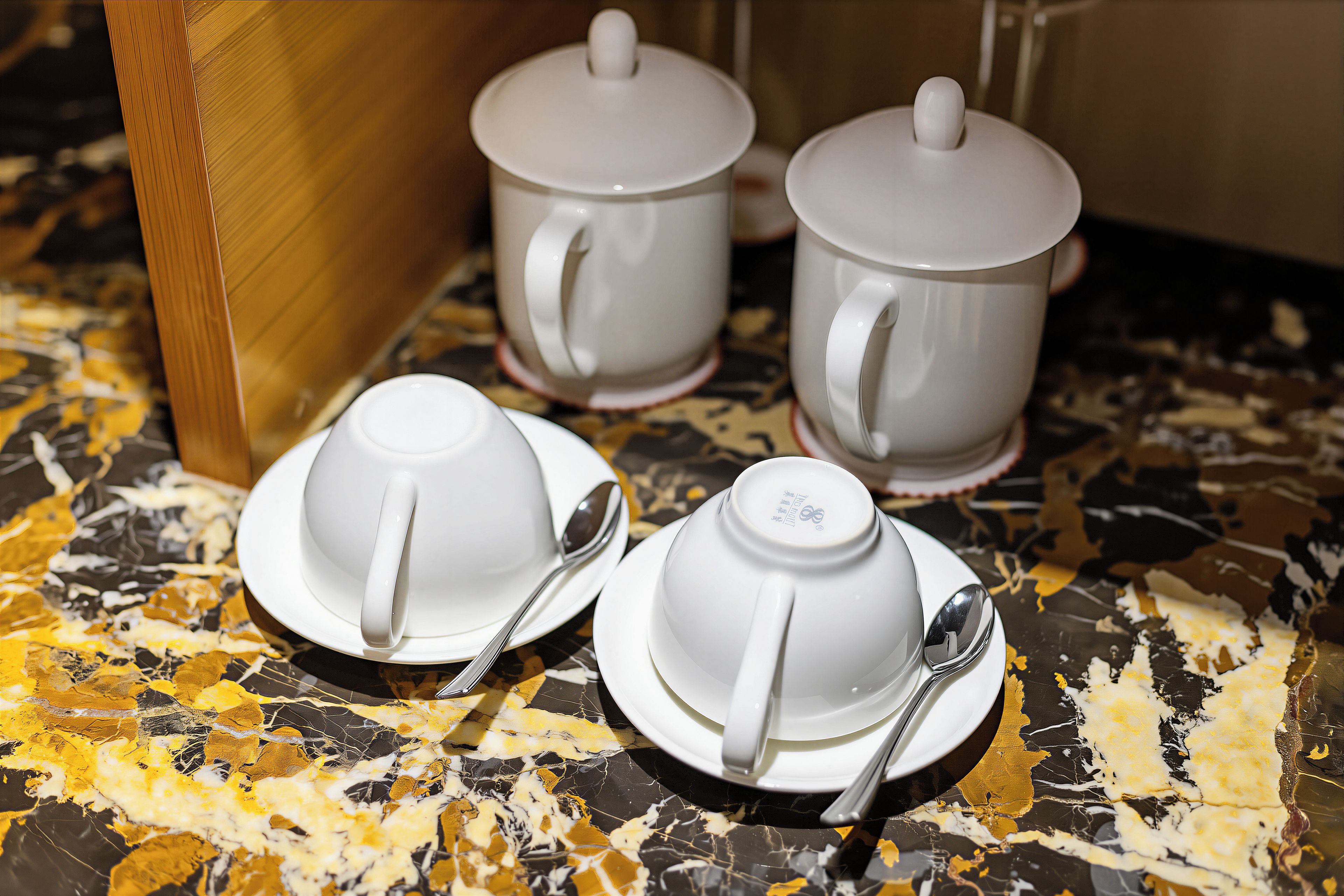 A set of white teacups and saucers with spoons on a marble table.