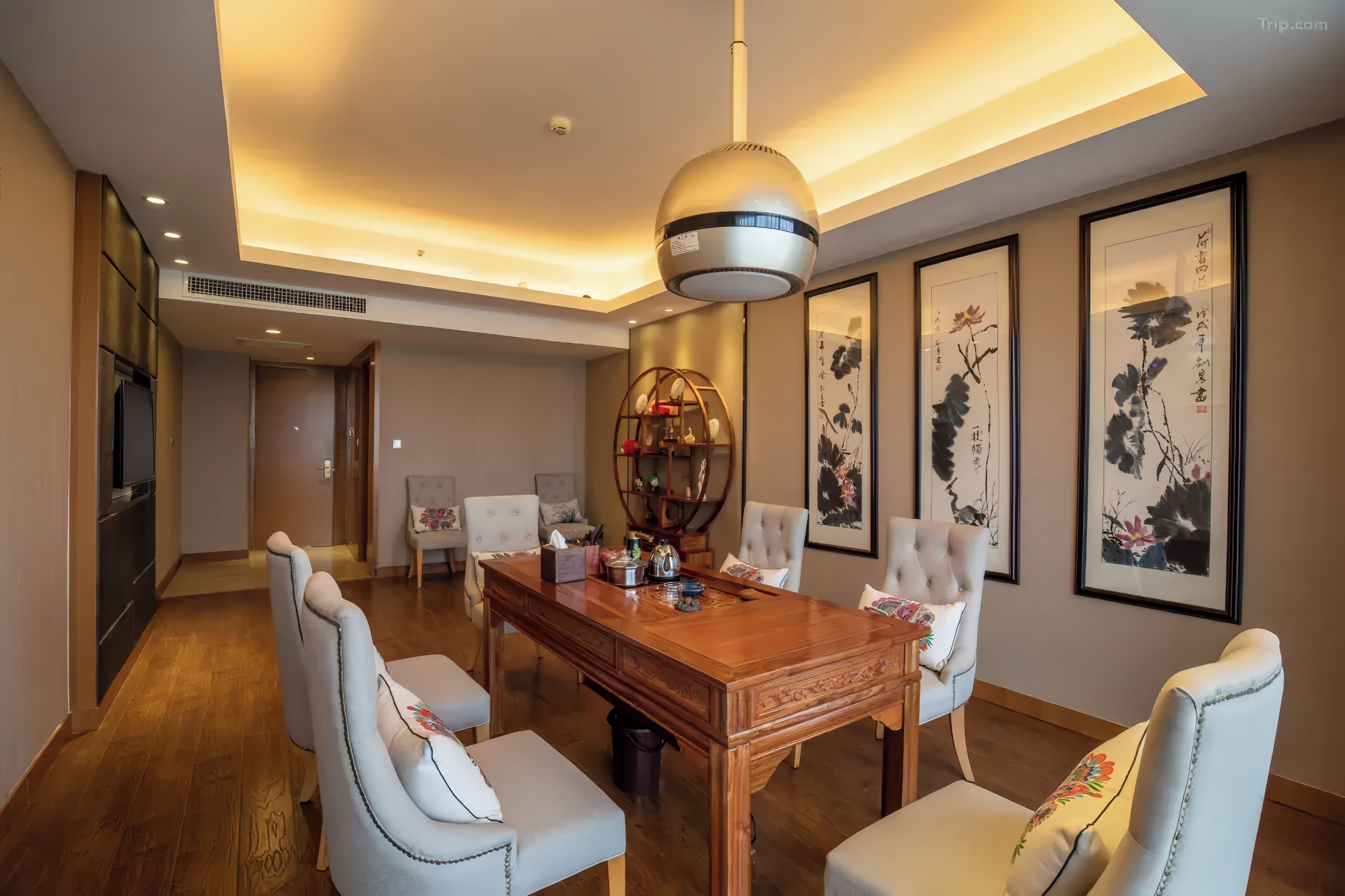 A dining area with a wooden table and white upholstered chairs, a hanging light fixture, and framed artwork on the walls.