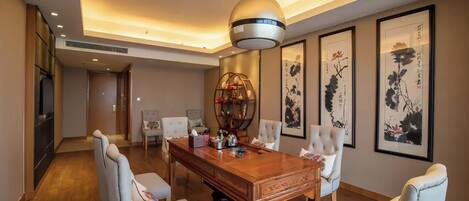 A dining area with a wooden table and white upholstered chairs, a hanging light fixture, and framed artwork on the walls.