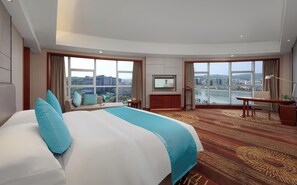 Quarto de hotel com uma cama grande, uma escrivaninha, televisão e vista para a paisagem urbana.