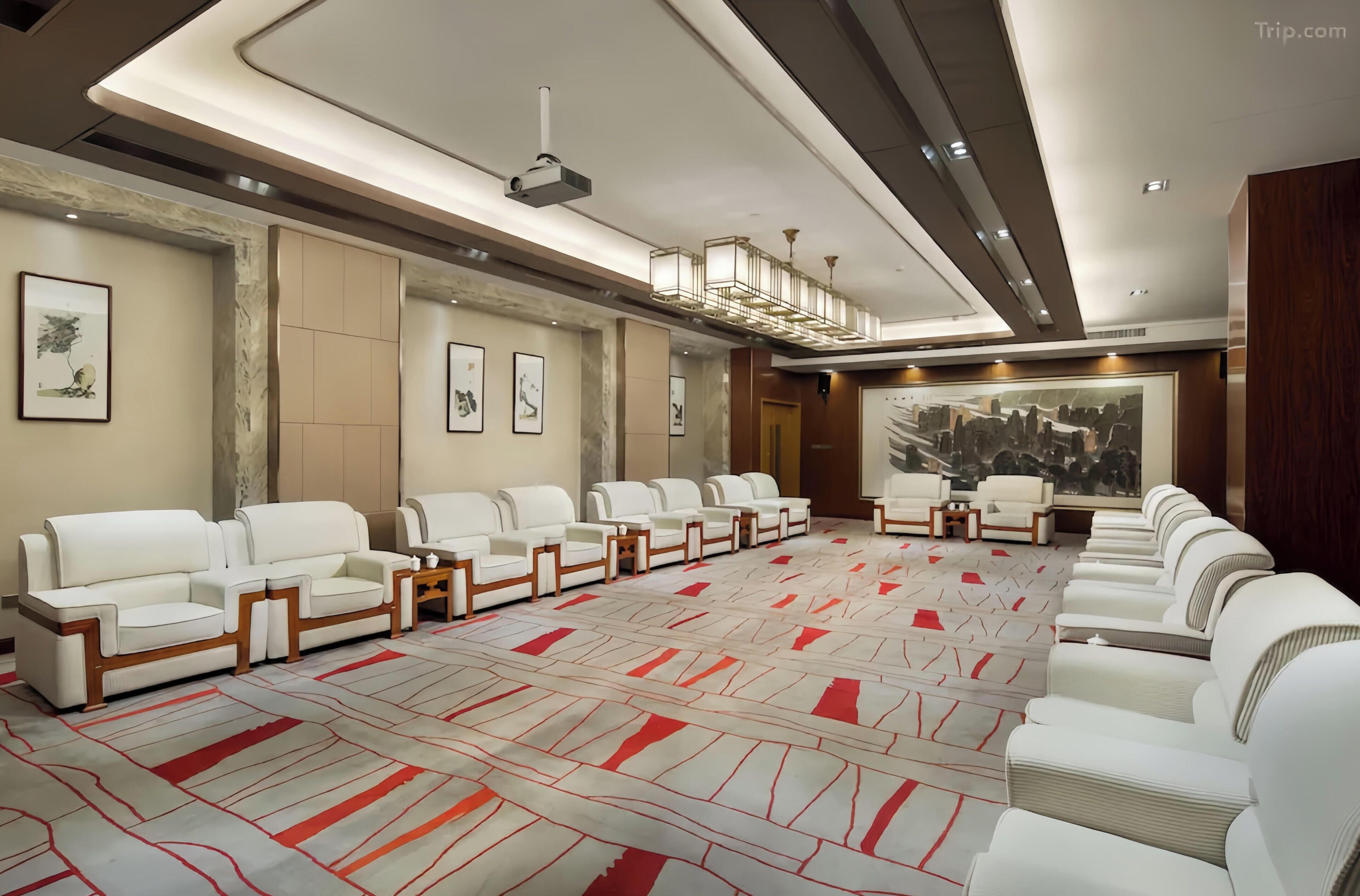 A conference room with white leather sofas arranged in a U-shape, a large carpet with red and white patterns, and a cityscape painting on the wall.