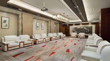 A conference room with white leather sofas arranged in a U-shape, a large carpet with red and white patterns, and a cityscape painting on the wall.