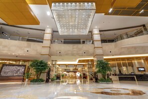 A spacious lobby with a large chandelier, multiple floors, and a reception desk. - King Maker Grand Hotel (Zhangjiajie)