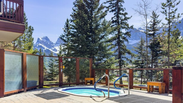 Zona de piscina con jacuzzi, terraza de madera y vistas a montañas.