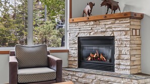 Una chimenea de piedra con fuego, un sillón de cuero marrón y vistas a árboles y edificios.