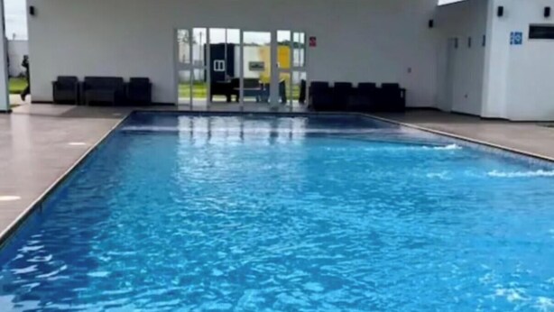 Une piscine avec une terrasse carrelée, un espace couvert avec des sièges et un bâtiment en arrière-plan.