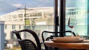 A table with a glass of wine, plates, and a chair in a restaurant with a view of a building. - Te Kaha View | Cozy New CBD 1BR (Christchurch)