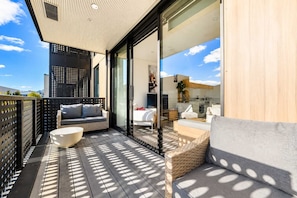 A modern outdoor balcony with a sofa, a round table, and a wicker chair. - Welles St | Christchurch CBD | Sleeps 4 | Balcony (Christchurch)