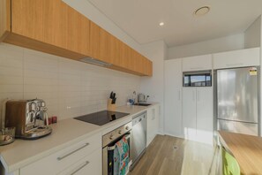 A modern kitchen with white cabinets, a stainless steel refrigerator, a built-in oven, and a coffee maker. - Modern Central City Sanctuary on Welles Street (Christchurch)